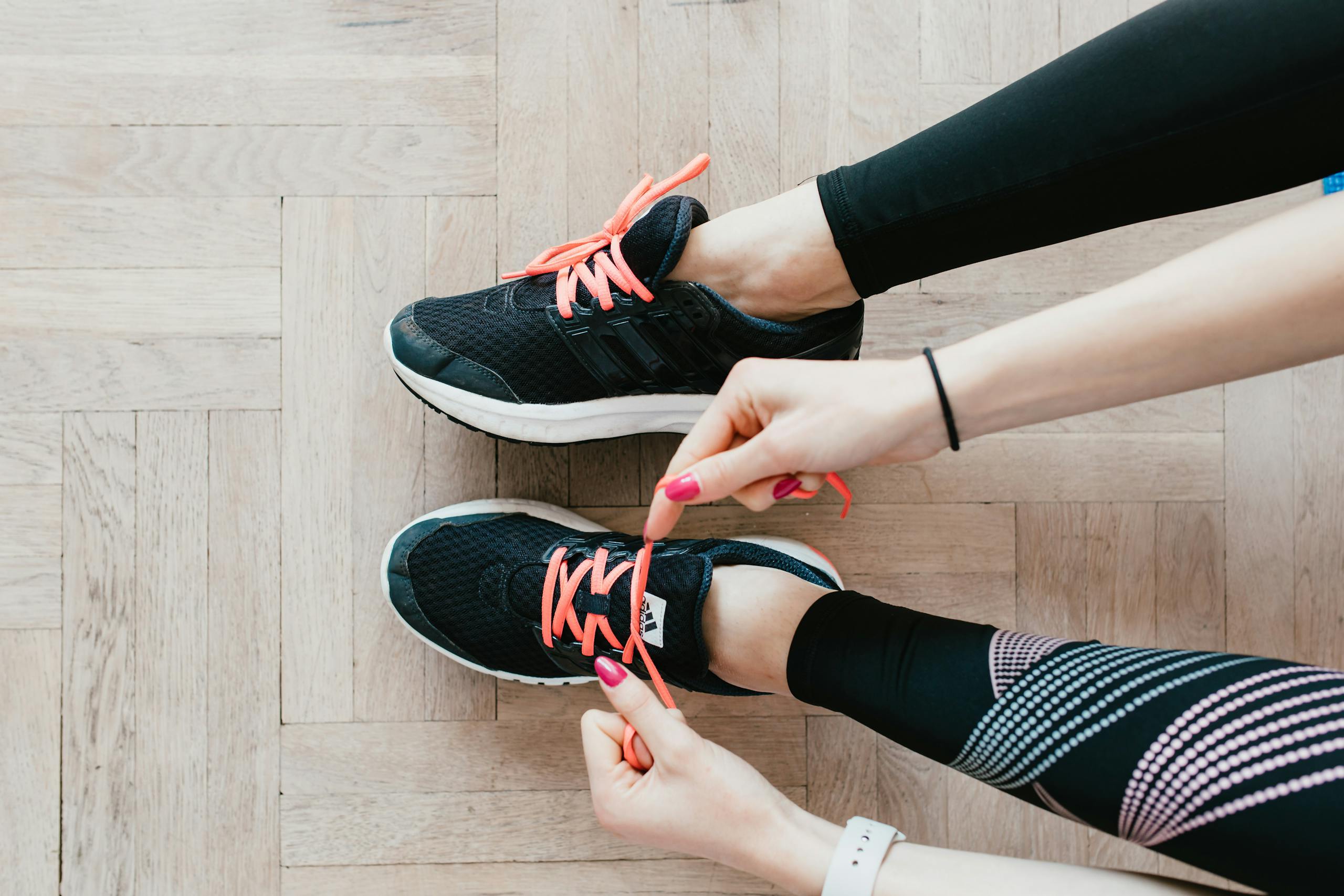 Leonie de Garnham: Coaching & Personal Training | Kickstart You | Close-up of a woman tying her sneakers, preparing for a home workout in leggings.